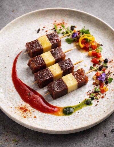 Plato gourmet con cuatro banderillas de atún y queso decorado con salsas.