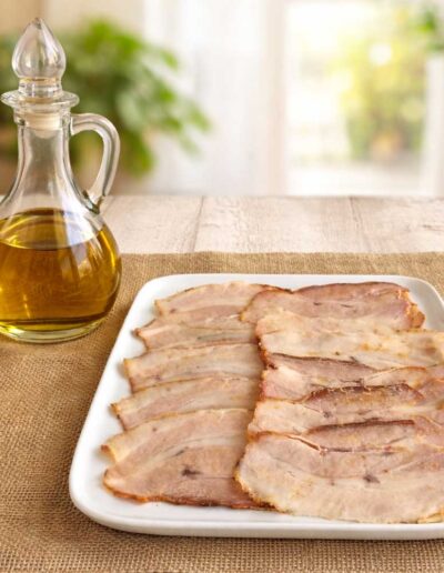 Plato blanco con finas lonchas de chicharrón junto a una aceitera de cristal.