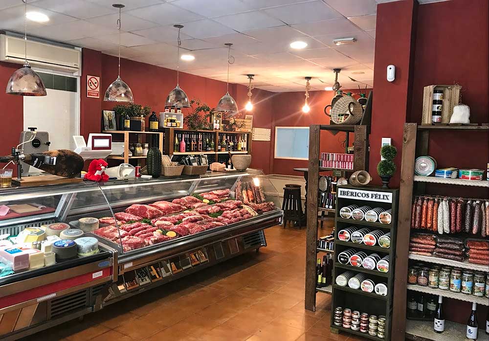 Interior de una tienda gourmet con vitrinas refrigeradas llenas de quesos, carne fresca y embutidos ibéricos.