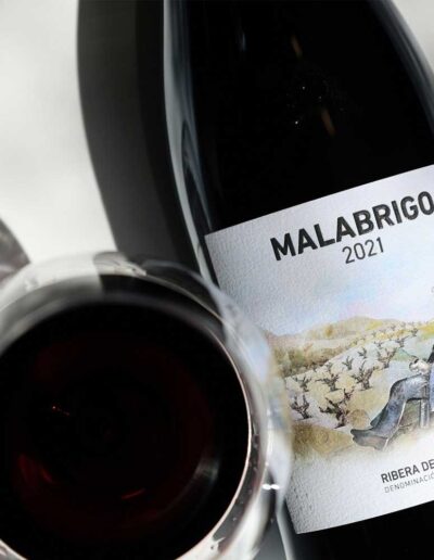 Primer plano de la etiqueta del vino tinto Malabrigo 2021 junto a una copa de vino tinto.